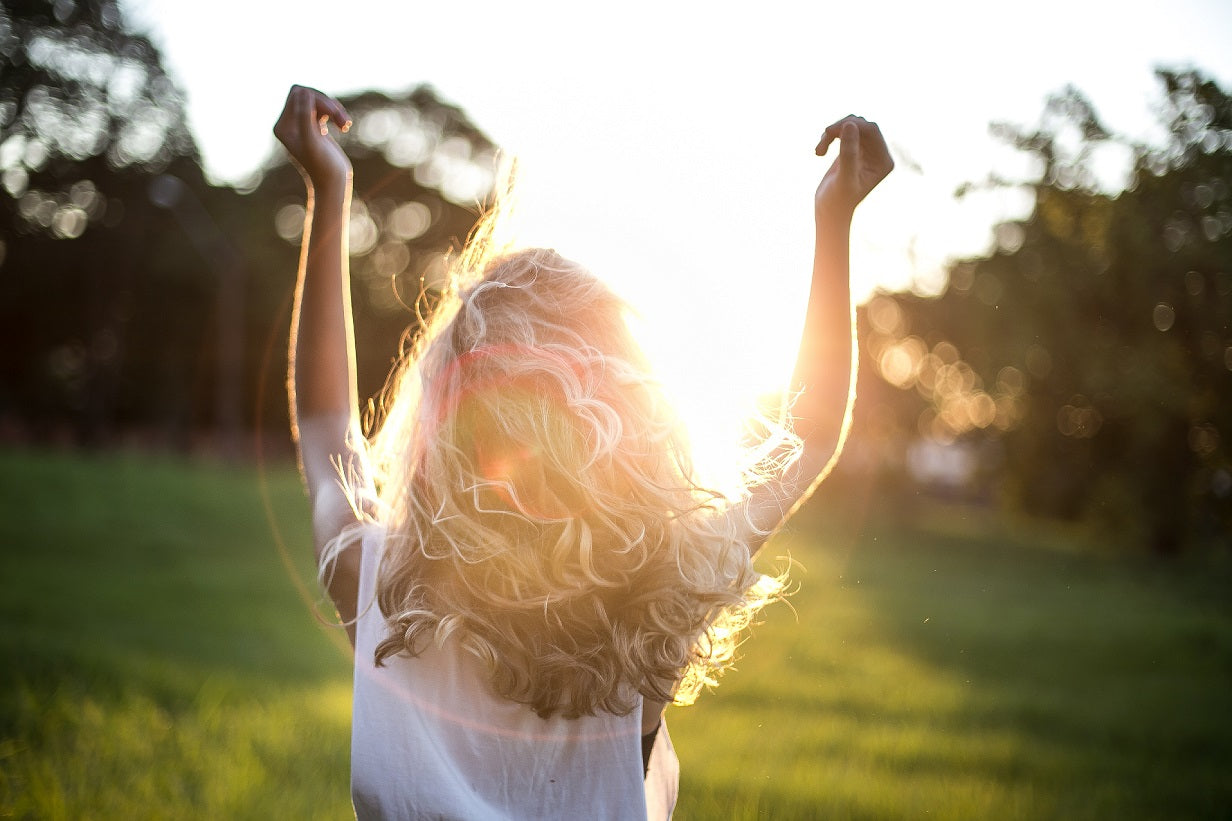 A woman joyfully raises her arms in celebration against a picturesque sunset backdrop.