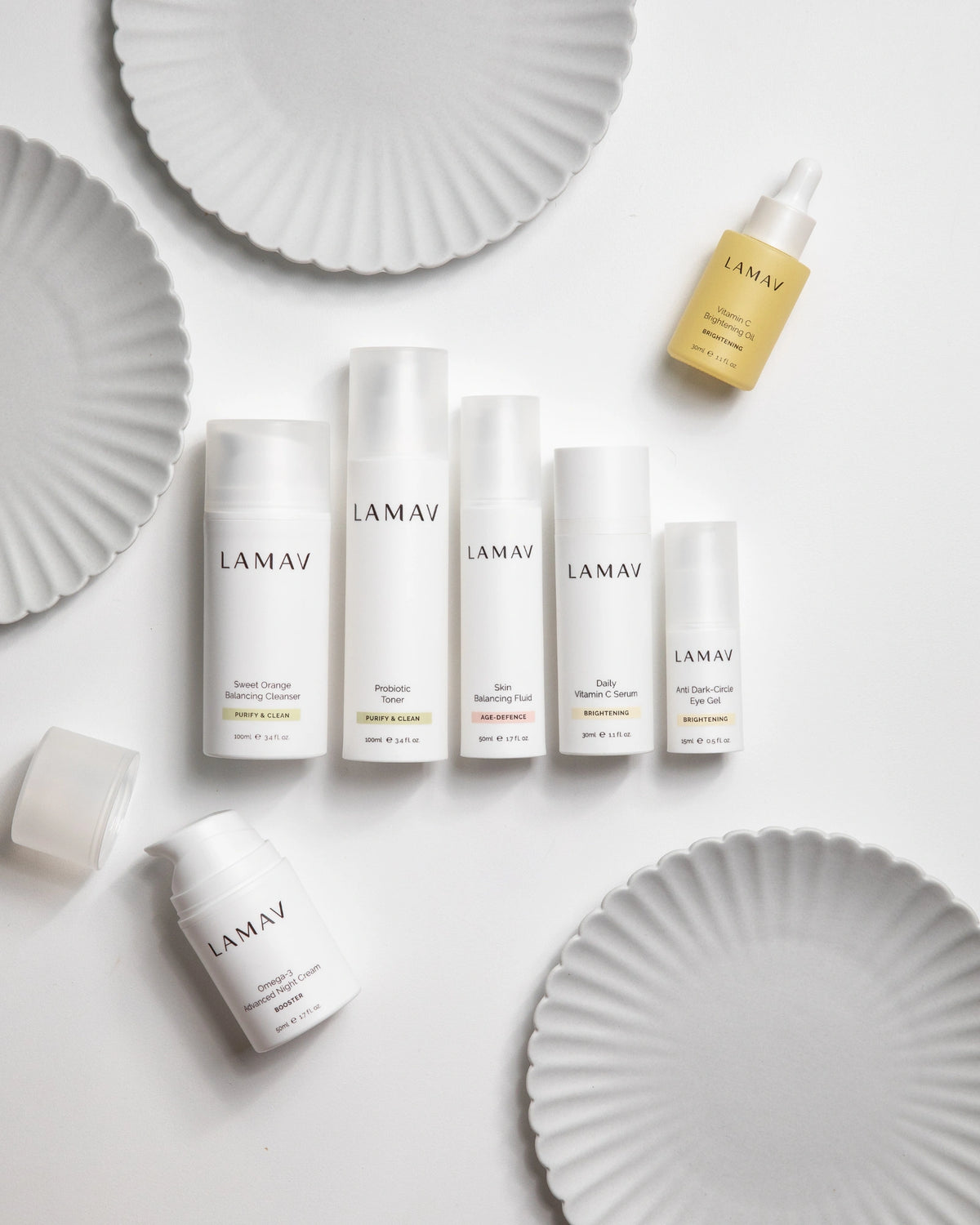 Age-Defence Collection by LAMAV — 7 bottles laid flat among white fluted plates | Complete routine for combination skin