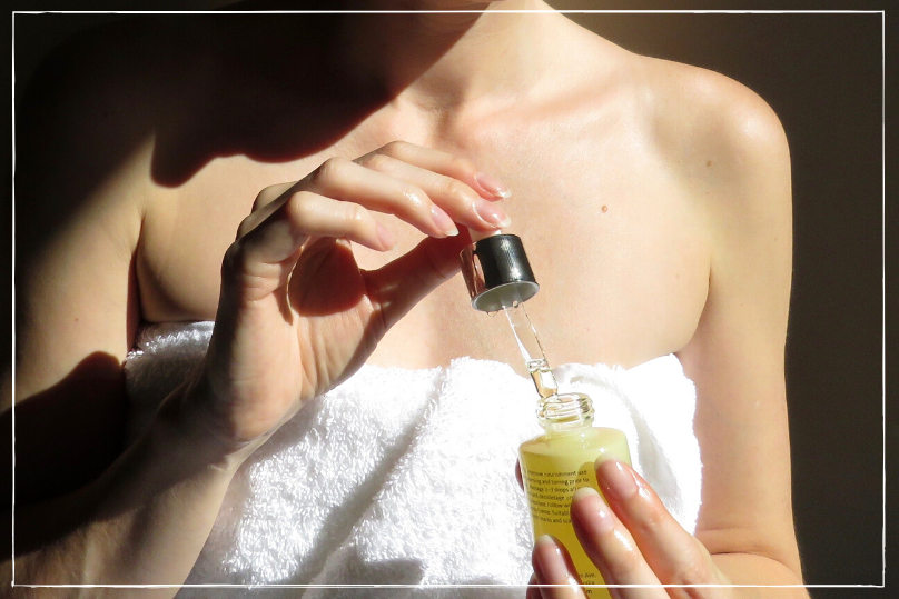  A woman in a towel, showcasing the benefits of organic skincare with a bottle of oil in hand.