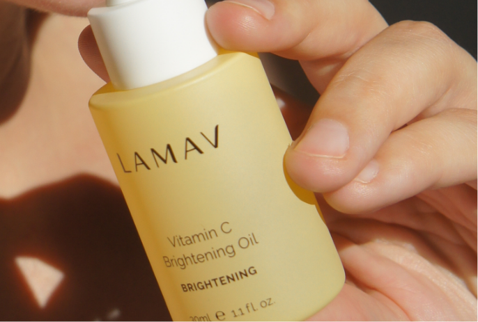 A woman holds a bottle of LAMAV Vitamin C brightening oil, promoting radiant skin with its nourishing properties.