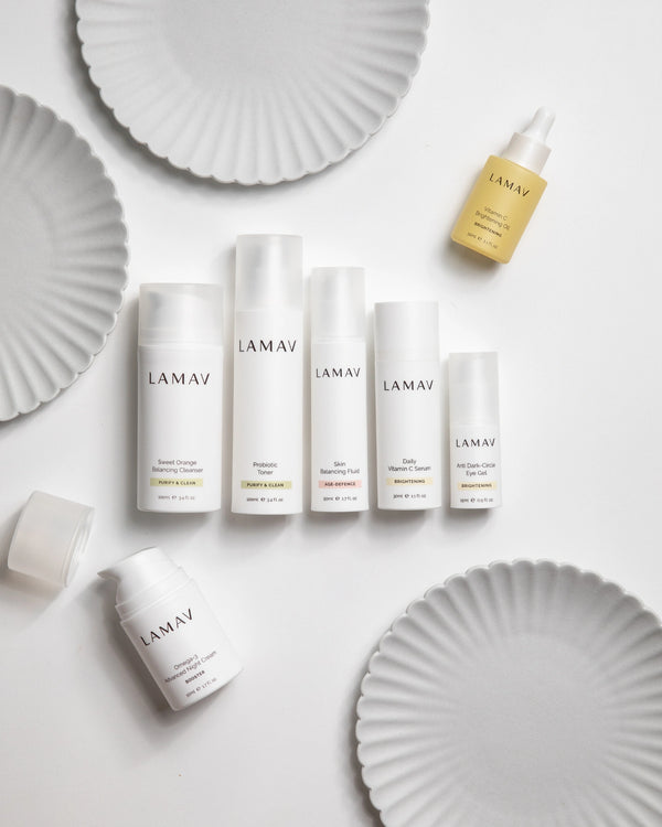 Age-Defence Collection by LAMAV — 7 bottles laid flat among white fluted plates | Complete routine for combination skin