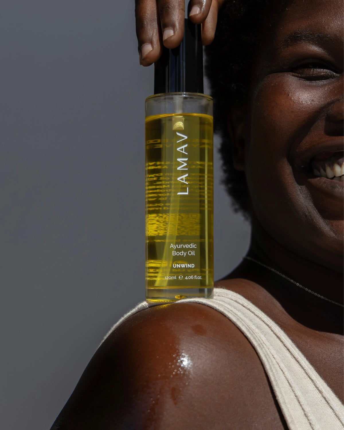 Ayurvedic Body Oil Unwind by LAMAV — smiling woman holding bottle on glowing shoulder | Hydrate and calm your body