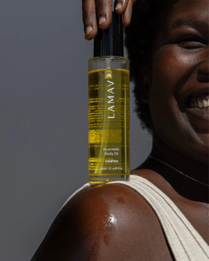 Ayurvedic Body Oil Unwind by LAMAV — smiling woman holding bottle on glowing shoulder | Hydrate and calm your body