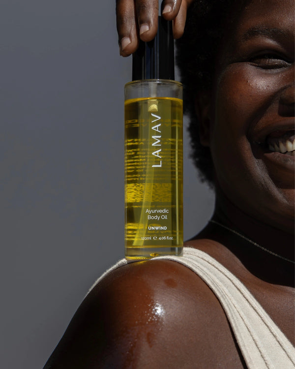 Ayurvedic Body Oil Unwind by LAMAV — smiling woman holding bottle on glowing shoulder | Hydrate and calm your body