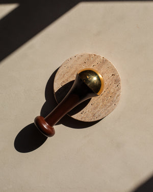 Ayurvedic Kansa Wand by LAMAV — resting on a round stone coaster | Releases facial muscle tension