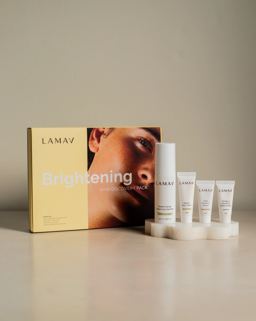 Brightening Discovery Pack by LAMAV — closed box and four products on a wavy white stone | visibly reduces dark spots.