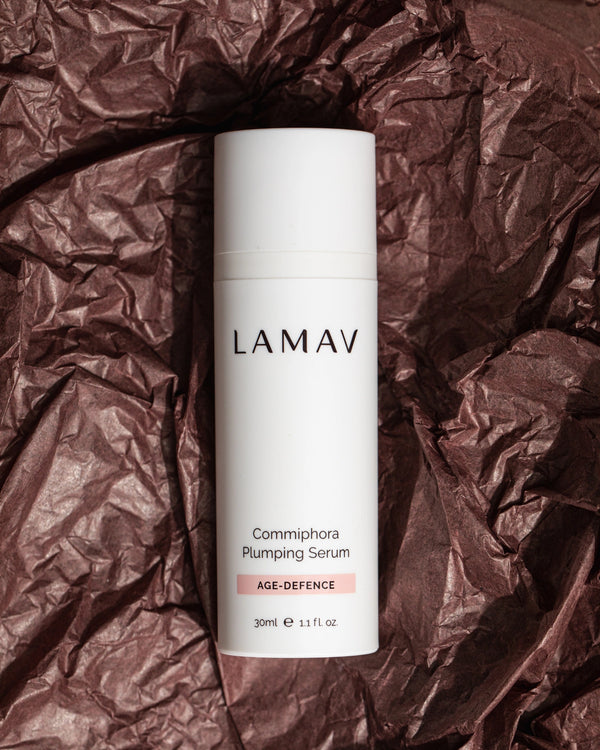 Commiphora Plumping Serum by LAMAV — bottle resting on dark crushed textured paper | boosts collagen and elasticity