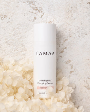Commiphora Plumping Serum by LAMAV — white bottle resting on soft white flowers | natural age defence formulation