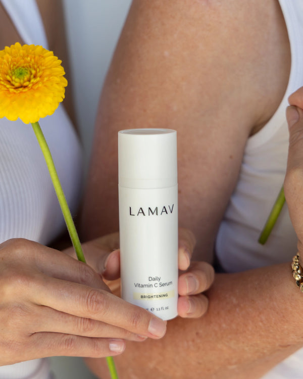 Daily Vitamin C Serum by LAMAV — hands holding the serum bottle alongside yellow flowers | Formulated for dull skin