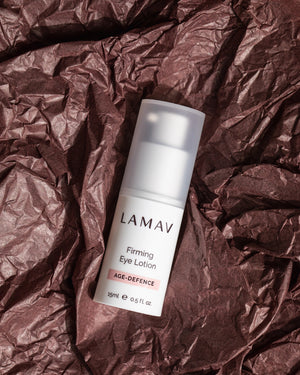 Firming Eye Lotion by LAMAV — bottle resting on dark crushed textured paper | natural anti-aging eye care