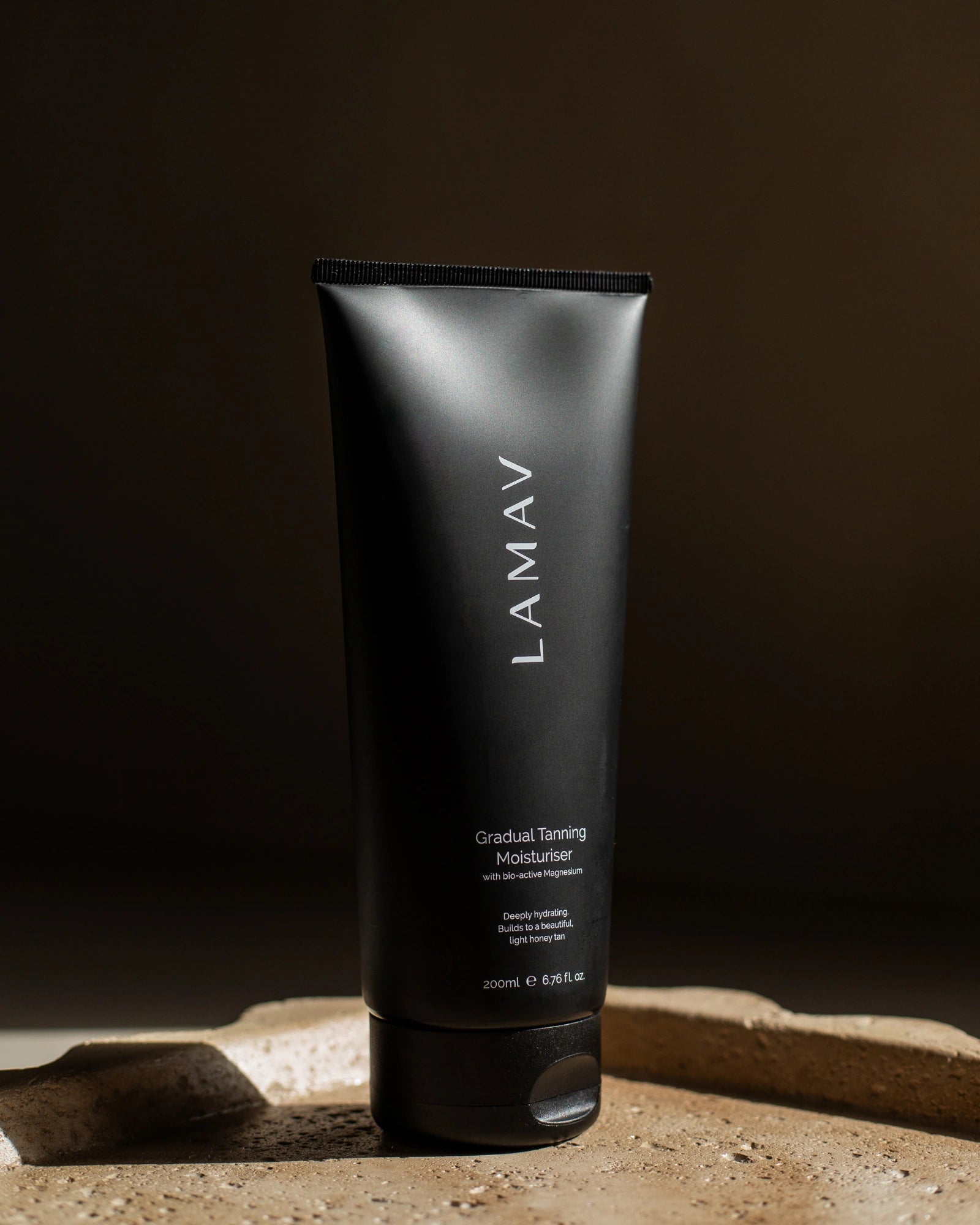 Gradual Tanning Moisturiser by LAMAV — black tube standing upright on a textured stone base | Develops a light honey tan
