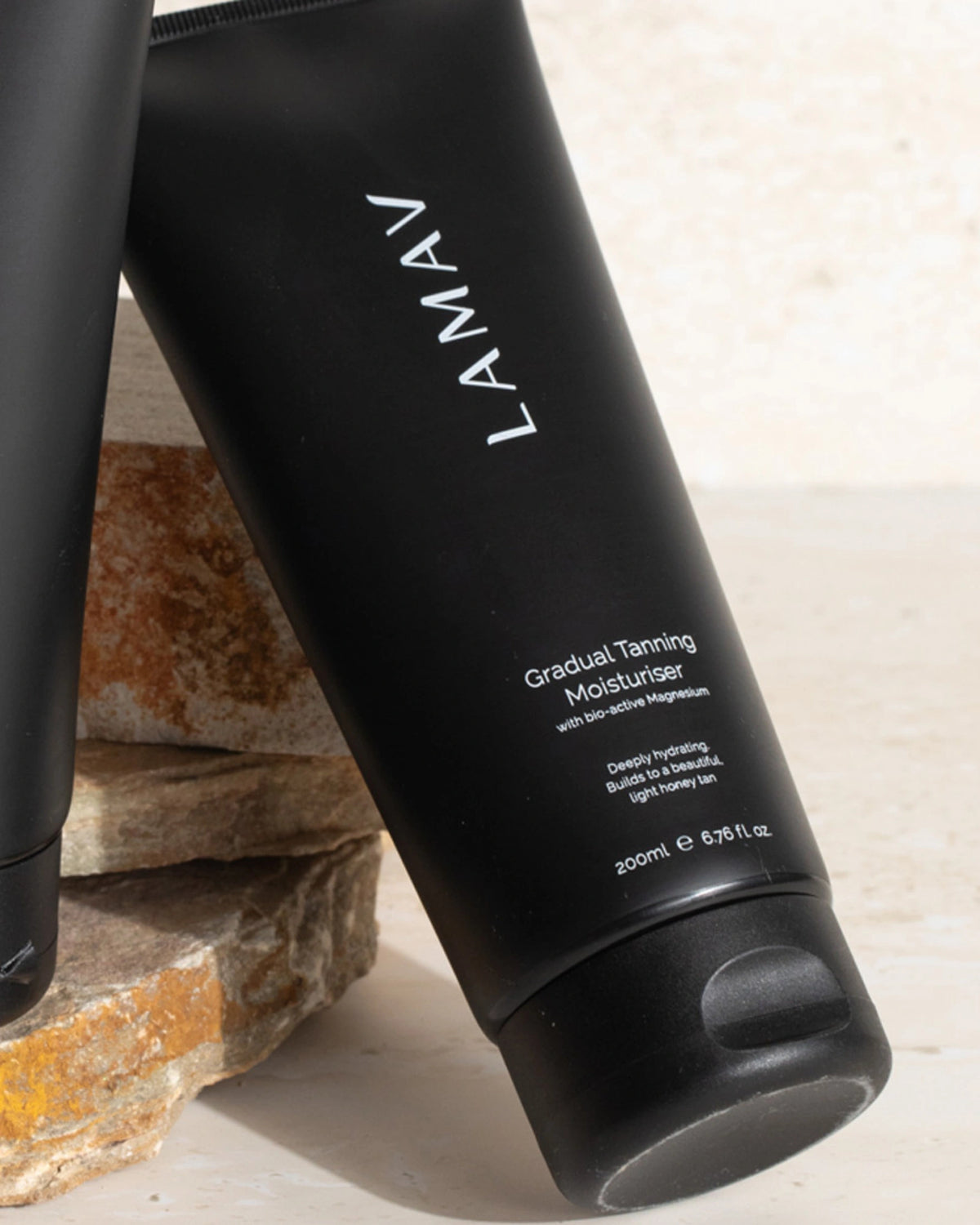 Gradual Tanning Moisturiser by LAMAV — black tube leaning against stacked natural stones | Nourishing daily self tanner