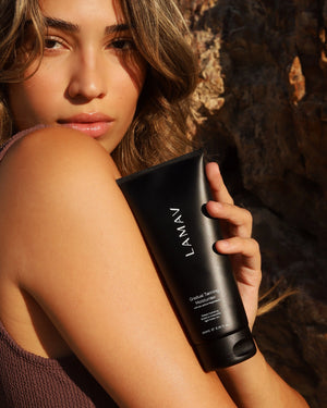 Gradual Tanning Moisturiser by LAMAV — woman holding the black tube against her arm outdoors | Builds a natural golden glow