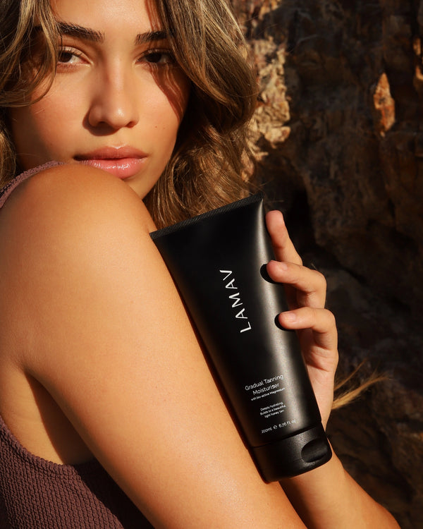 Gradual Tanning Moisturiser by LAMAV — woman holding the black tube against her arm outdoors | Builds a natural golden glow