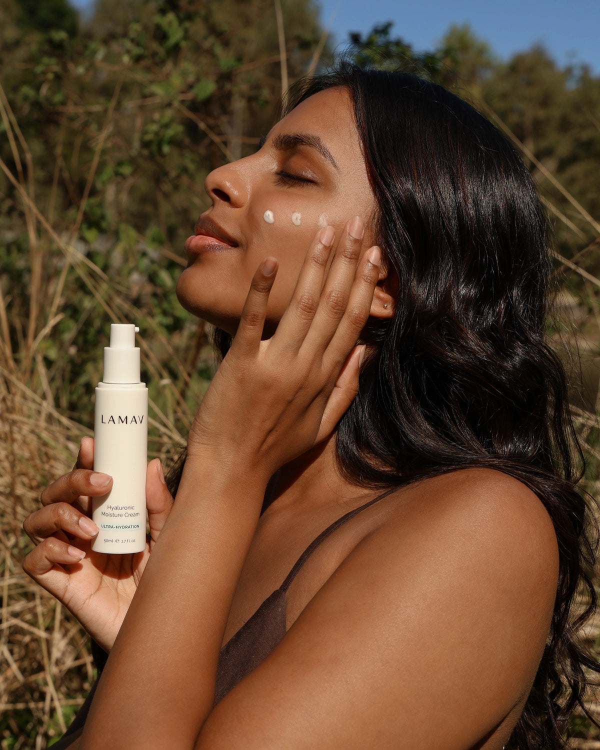 Hyaluronic Moisture Cream by LAMAV — Woman outdoors applying cream to cheek holding 50ml bottle | Deep hydrating glow
