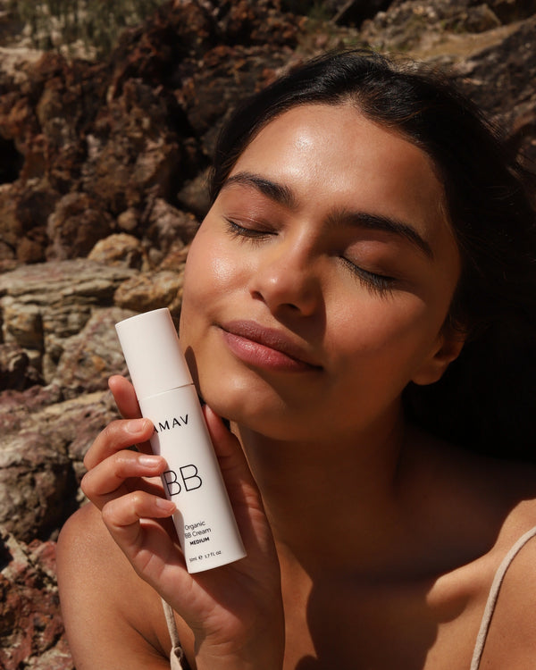 Organic BB Cream by LAMAV — radiant woman with closed eyes holding Medium bottle by rocks | sun-kissed, natural-looking glow.