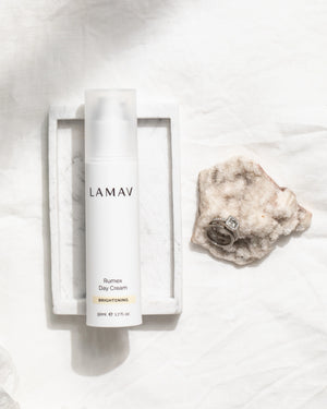 Rumex Advanced Lightening Cream by LAMAV — bottle in tray next to rings on stone | fading dark spots