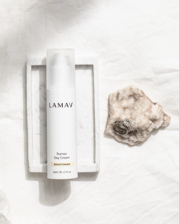 Rumex Advanced Lightening Cream by LAMAV — bottle in tray next to rings on stone | fading dark spots