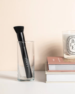 Vegan Foundation Brush by LAMAV — standing in a clear glass next to books | perfectly blends organic foundation